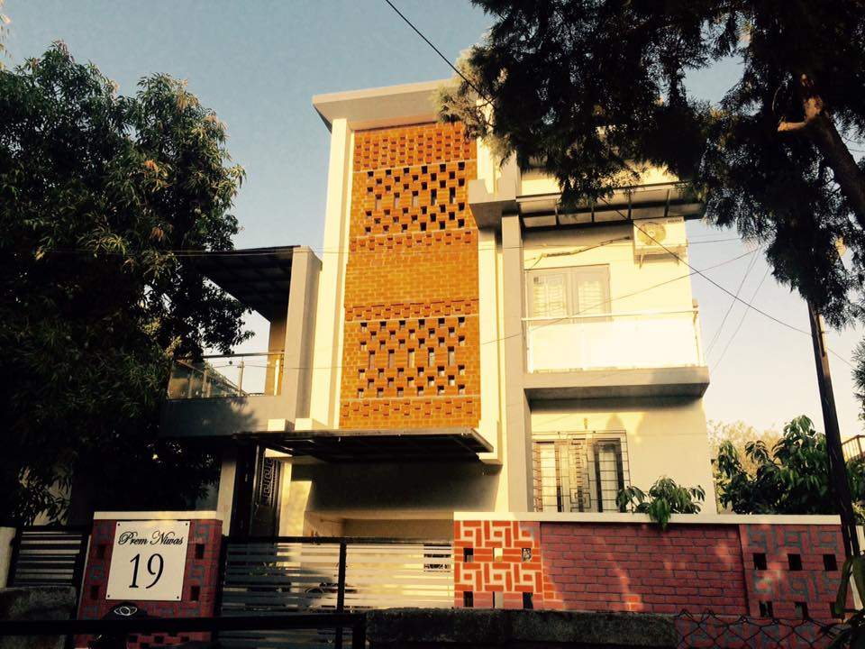 3 Storeyed Bungalow with an Exposed Brick Patterned Facade a Compound Wall a Balcony on one Side with Glass Railings