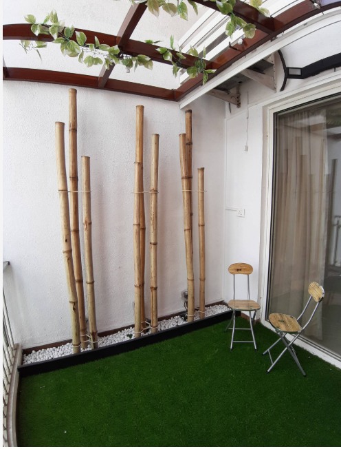 Balcony-designed-with-Artificial-Grass-Mat-on-the-Floor-with-Pedestal-Statue-of-Buddha-in-White-Bamboo-Sticks-on-one-side-over-White-Pebbles-tied-with-a-Thread