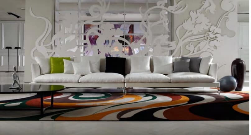 4-Seater White Upholstered Sofa having Metal Legs & Colourful Cushions is nicely placed with the White Jali Partition behind it, with a colourful Floor Rug highlighting the Floor