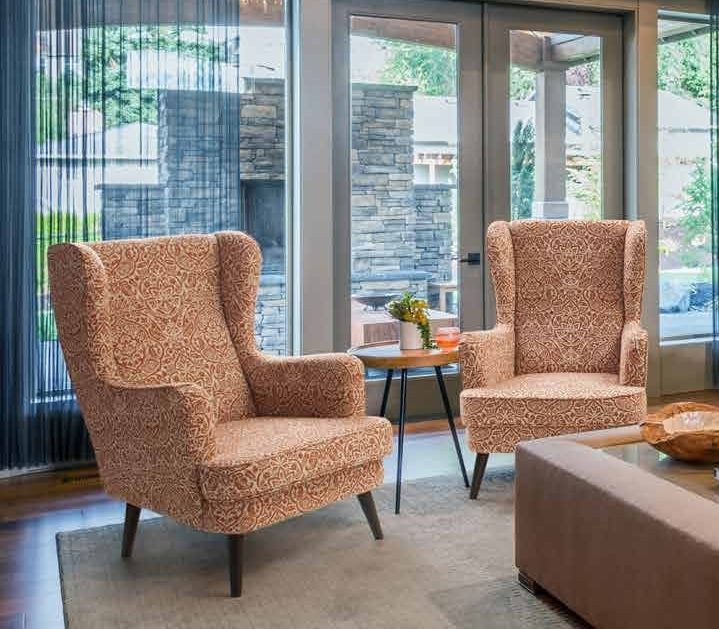 The Printed Floral Upholstered Wingback Chairs with Wooden Legs are Nicely Place at the Glass Facade